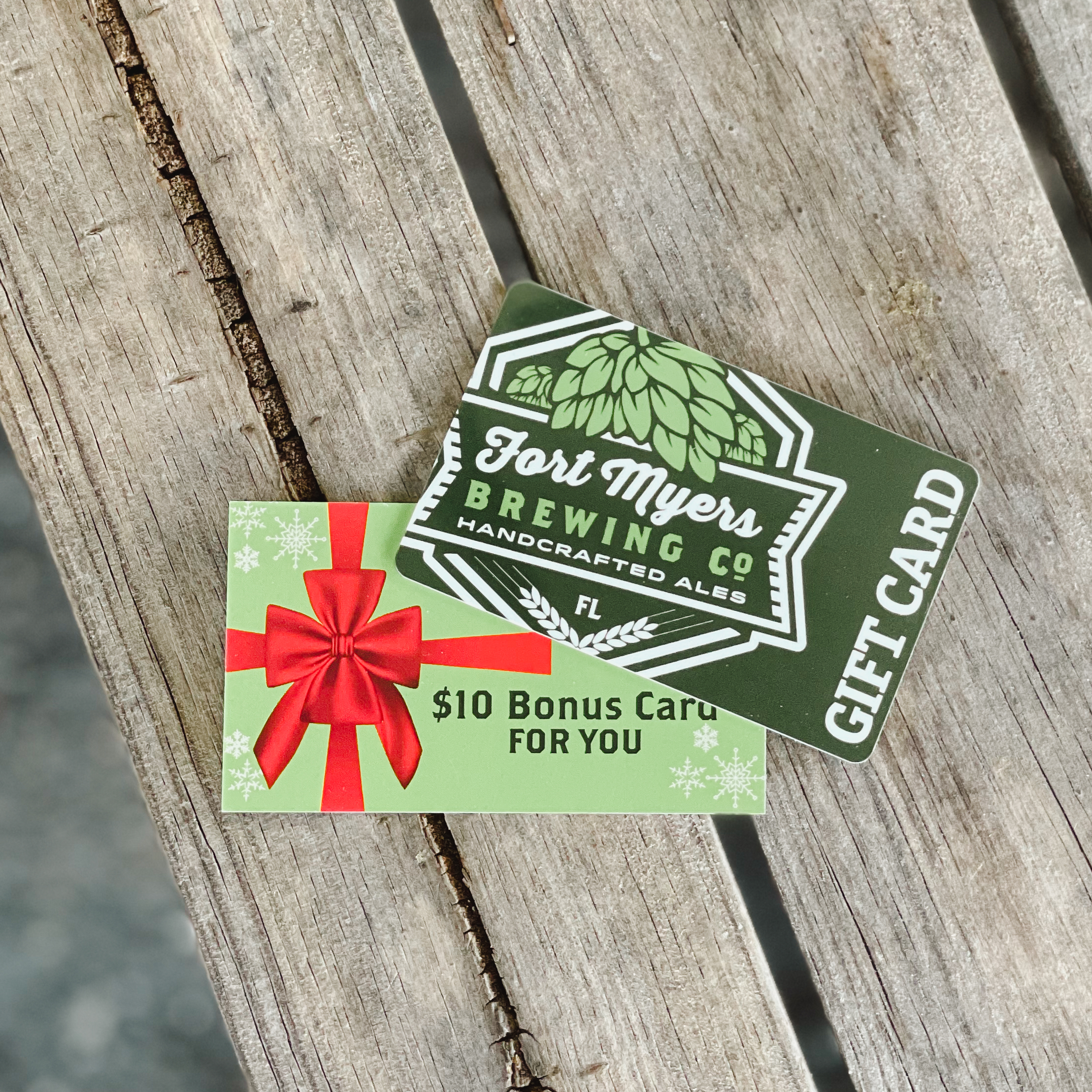 A Fort Myers Brewing gift card with a bow on it sitting on a wooden table.
